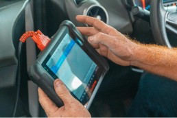 A mechanic performing engine diagnostic testing on a car in an auto repair shop.
